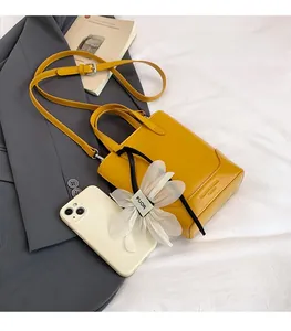 Detailansicht der kleinen gelben Umhängetasche aus Leder mit Blumenanhänger und Handy-Vergleich