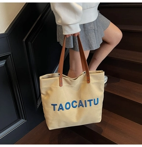 Close-up of durable canvas tote bag with blue embroidery and brown leather handles