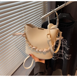 Détail du sac seau crème avec texture litchi, finitions dorées et poignée en foulard
