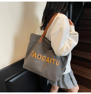 Detail of grey canvas tote bag with orange embroidery and brown leather shoulder straps