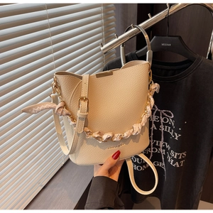 Détail du sac seau beige avec poignée en chaîne enrubannée de soie et fermoir doré