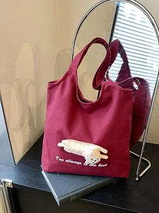 Burgundy canvas tote bag with cute plush doll and white embroidery in a lifestyle setting