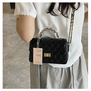 Detail of black quilted crossbody bag with gold twist lock and leather chain strap on model