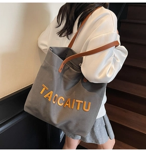 Close-up of grey canvas tote with orange embroidery and leather handles on a model