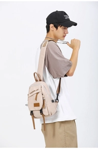Rear view of a light beige crossbody sling bag with leather accents on a male model