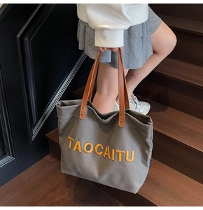 Close-up of charcoal canvas tote bag featuring orange TAOCAITU embroidery and leather handles