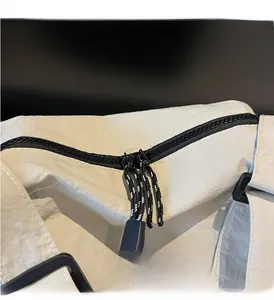 Close-up of dual black zippers and RANATU logo on cream nylon crossbody shoulder bag