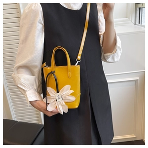 Detail einer gelben Lackleder-Mini-Tote-Bag mit einem weißen Gänseblümchen-Anhänger