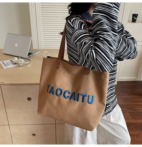 Large brown canvas tote bag with blue embroidery detail and brown leather straps