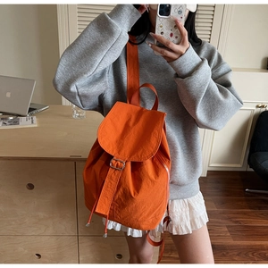 Détail du sac à dos orange en nylon avec fermeture à rabat et boucle métallique