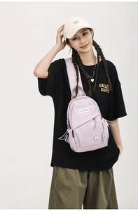Detail view of light purple canvas chest bag with zipper compartments and brand logo