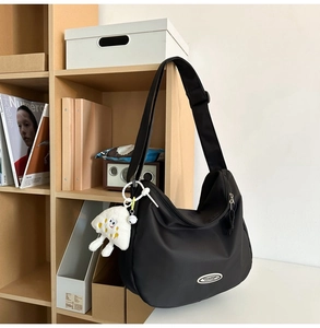 Close-up of black nylon crescent bag featuring a white cloud plush charm on a wooden shelf