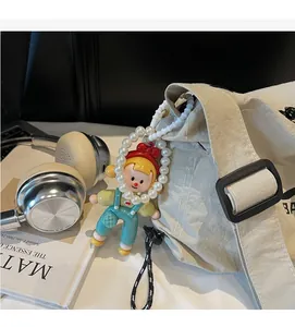 Detail of cartoon girl charm with red bow and pearl chain on a beige nylon bag