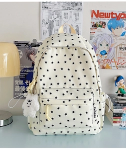 Close-up of beige canvas backpack featuring black star patterns and a plush monster charm