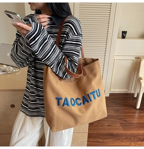 Detail of large canvas tote bag with blue embroidered letters and leather strap