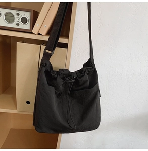 Detail of black nylon drawstring bucket bag with side pockets on a wooden bookshelf