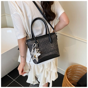 Détail d'un sac cabas texturé gris foncé avec breloques porté par un mannequin femme