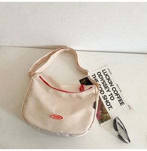Detail of off-white nylon crescent bag showing red zipper and brand logo on table