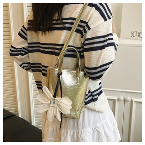 Detail der metallisch-goldenen Mini-Tote-Tasche mit Struktur und Blumenanhänger