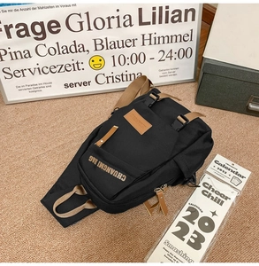 Detail of black canvas crossbody chest bag with brown leather accents and dual buckles