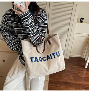 Detailed view of canvas tote bag with brown leather straps and blue TAOCAITU embroidery