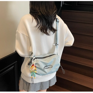 Detail of light blue nylon crossbody bag with black logo and cute cartoon doll pendant