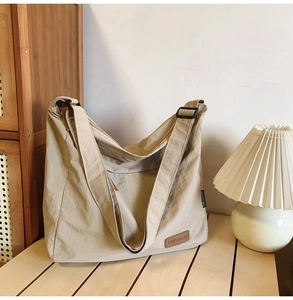 Close-up of beige nylon messenger bag with CHUANGMI leather label on a wooden table