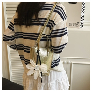 Detail der metallisch goldenen Mini-Tasche mit Gänseblümchen-Anhänger und Glanzstruktur