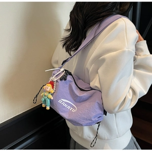 Detail of purple nylon dumpling bag with pearl chain and doll mascot on a model