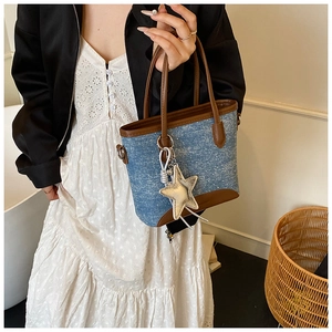 Détail du sac cabas en denim bleu avec finitions en cuir marron et breloque étoile