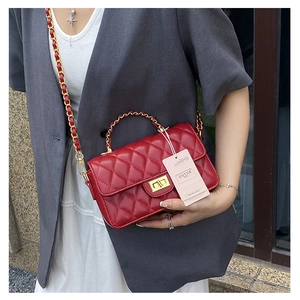 Detail view of red quilted chain crossbody bag with golden twist lock on grey blazer