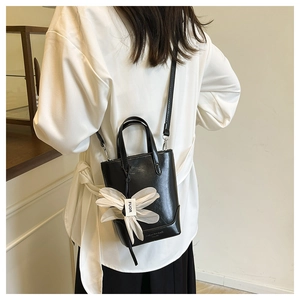 Details der schwarzen PU-Lederhandtasche mit weißer Stoffblume und Logo-Prägung