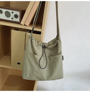 Detail of light green nylon drawstring bucket bag with two front pockets on a wooden shelf