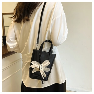Detail einer schwarzen Mini-Handtasche aus Leder mit weißer Schleife und FUOR-Anhänger