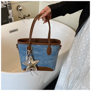 Détail du sac cabas en denim avec garniture en cuir marron et pendentif étoile argenté