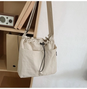 Detail of cream drawstring bucket bag showing front pockets and nylon texture in a home setting