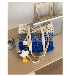 Detail of a handmade knit tote bag in blue and beige with a cute duck charm on a desk