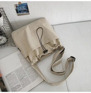 Detail of beige nylon crossbody bag with black drawstring closure and adjustable strap
