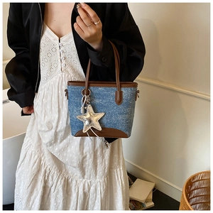 Sac seau en denim bleu avec bordure en cuir marron et breloque étoile tenu par un mannequin