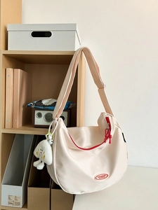 Off-white nylon crescent bag with red accents and cloud plush charm on wooden shelf