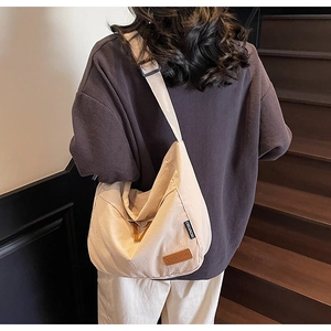 Détail du sac bandoulière en toile beige avec étiquettes de marque et sangle réglable