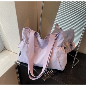 Detail of lavender nylon tote bag featuring adjustable side drawstrings and logo tag