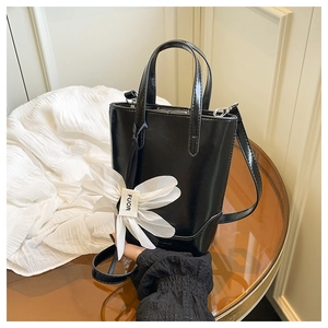 Detail der schwarzen Mini-Eimertasche mit großem weißem Blumenanhänger und Glanzeffekt