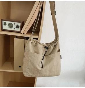 Detail of khaki nylon crossbody bag showing drawstring closure and front pockets on a shelf