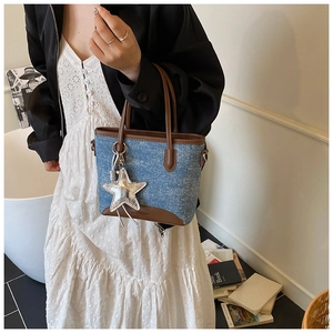 Détail du sac seau en denim bleu avec bordure en cuir marron et breloque étoile argentée