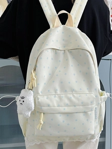 Minimalist beige backpack with blue star patterns and white plush charm on a black outfit