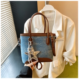 Détail du sac cabas en denim bleu avec base en cuir marron et breloque étoile