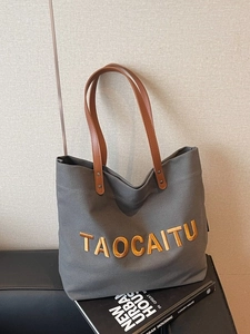 Large dark grey canvas tote bag with brown leather handles on a black leather sofa