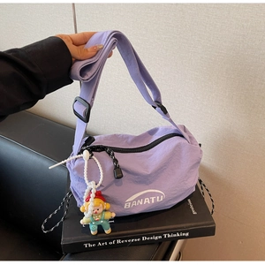 Close-up of purple nylon crossbody bag with logo, zipper detail, and cute girl pendant charm