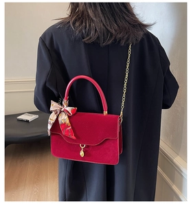 Detail of red velvet handbag featuring gold chain strap and decorative silk scarf